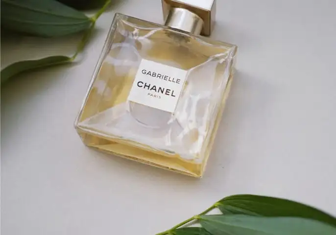 A Gabrielle perfume bottle lies on a white background surrounding by some leaves
